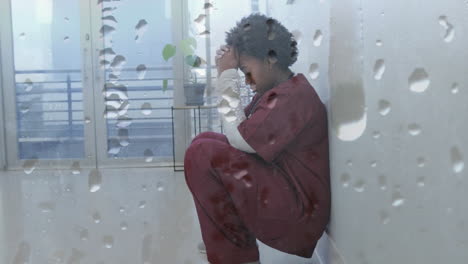 animation of water droplets over unhappy african american female doctor crouching in corridor