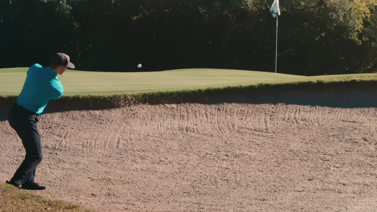 Slow-motion strike from a sand trap sends the ball onto the green beside the flag, capturing clean contact and rising sand. Male golfer