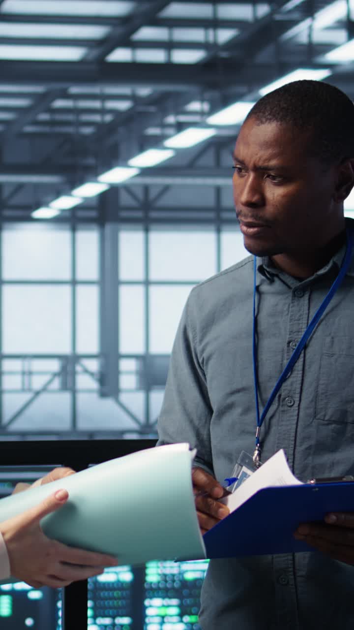 Vertical video Data center engineer greeting colleague, examining system diagnostics paperwork