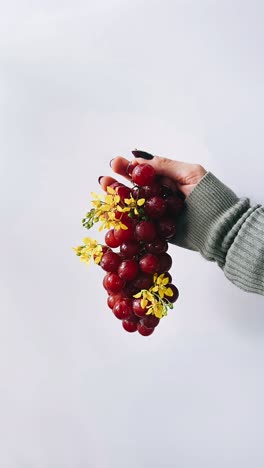 hand holding bunch of red grapes with flowers