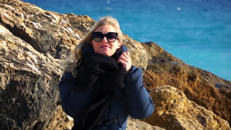 Close-up-of-a-young-woman-enjoying-the-seaside,-the-blue-sea-in-soft-focus-in-the-background-SLOMO