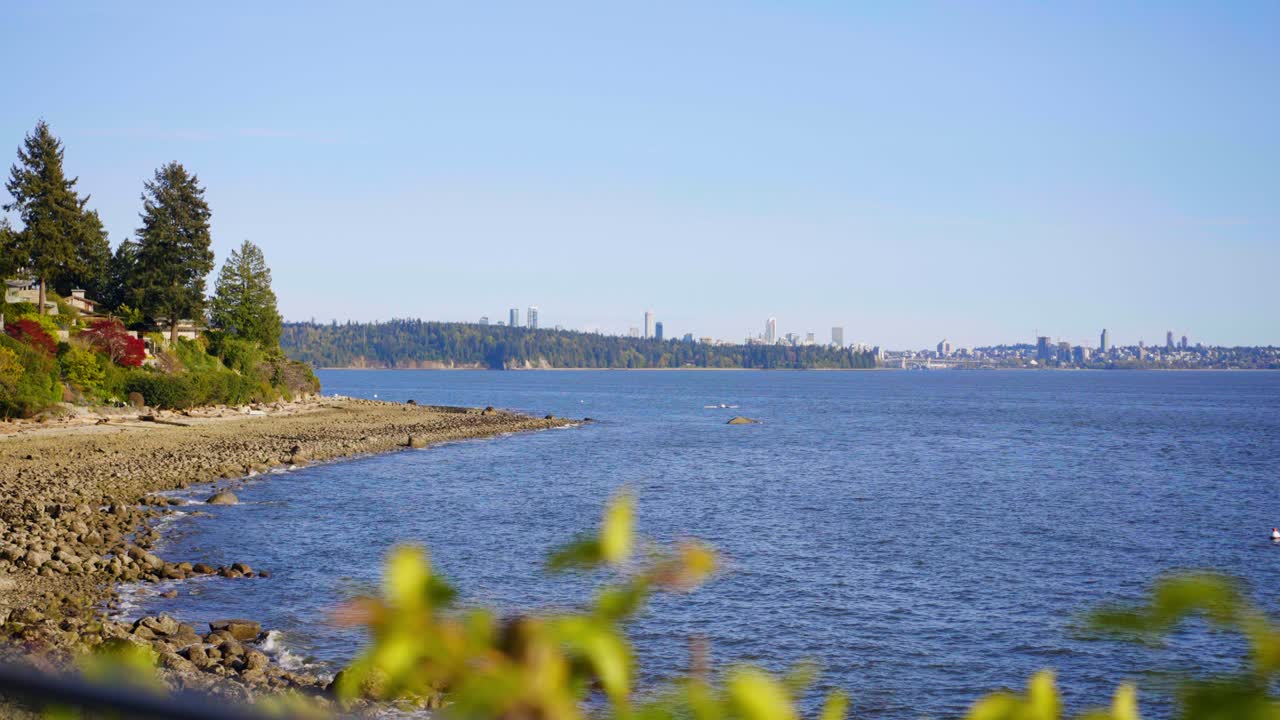 A scenic shot of the beach and the blue waters of the sea in West Vancouver, Canada with Vancouver City over on the horizon