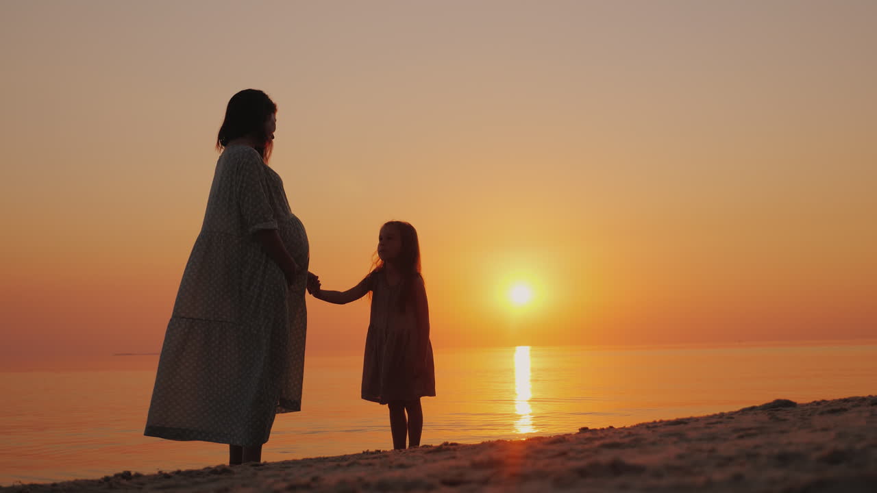 silueta de una mujer embarazada con un bebé cerca de pie cerca del mar al atardecer esperando el seco