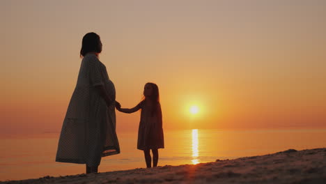 silhouette of a pregnant woman with a baby near by stand near the sea at sunset waiting for the seco