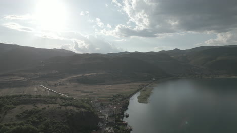 Drohnenschuss-Von-Oben-In-Albanien,-Der-An-Einem-Bewölkten-Tag-Rückwärts-Fliegt,-Während-Die-Sonne-Durch-Die-Wolken-Kommt-Und-Land-Und-Wasser-Unter-Dem-Baumstamm-Liegen