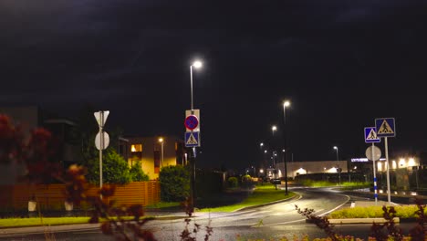 static nighttime shot on a quiet suburban street while flashes of lightning in the night sky. forks of lightning flash across the dark dense storm clouds. streetlights illuminate the wet asphalt road