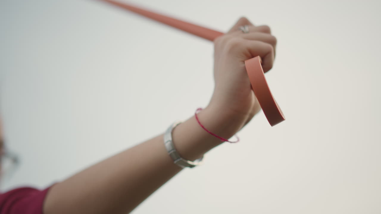 Hand Gripping Red Ribbon Against Sky, Closeup Of Female Wrist With Bracelet And Ring, Gentle Wind Causing Subtle Ribbon Flutter, Overcast Pastel Sky Creating Calm Minimalist Mood, Sense Of Upward