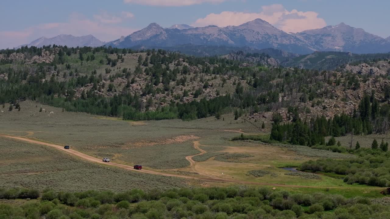 un vasto paisaje de campos y altas montañas capturado desde arriba en la cordillera del río wind de wyoming con suv conduciendo a lo largo de carreteras de tierra