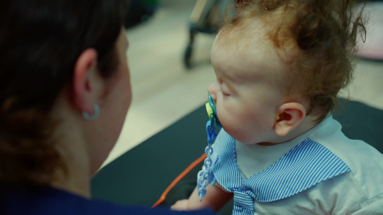 Madre che tiene in braccio il suo neonato con un vestito a righe, che usa un ciuccio e riposa comodamente in una culla