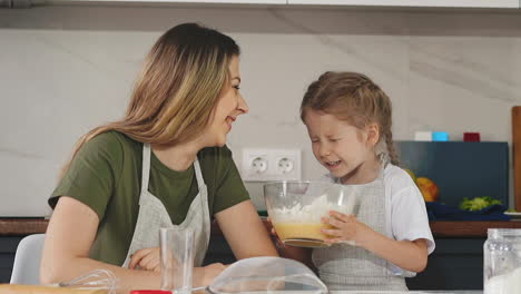 daughter and mother in aprons in kitchen having fun