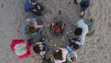 Drohnenaufnahme-Einer-Familie-Aus-Mehreren-Generationen,-Die-Im-Winterlichen-Strandurlaub-Marshmallows-Am-Feuer-Toastet