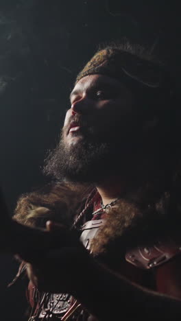ecstatic young shaman in altai ethnic costume and swirling smoke on dark background slow motion. spiritual traditions of siberian folks