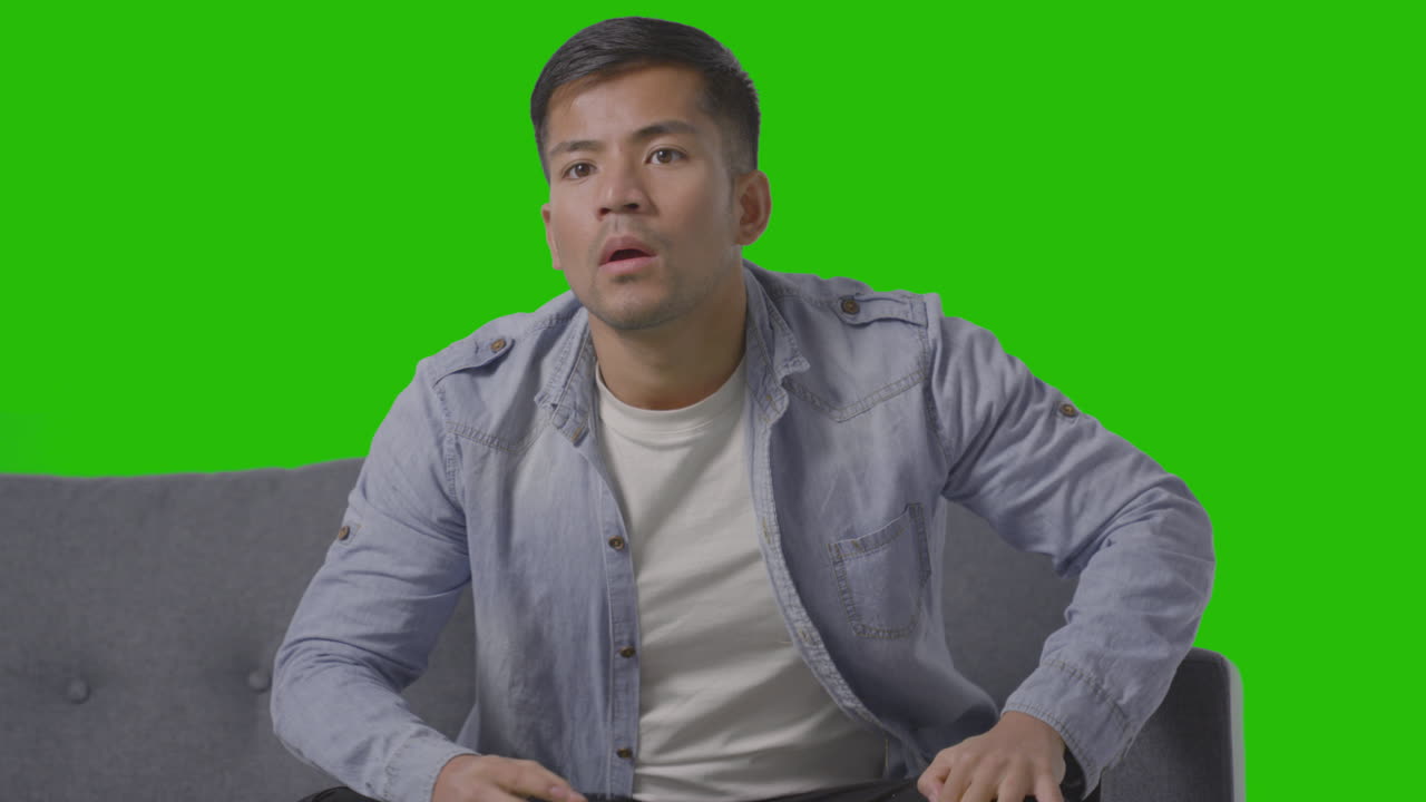 녹색 화면 2에 대해 tv에서 스포츠를 보고 소파에 앉아 실망한 청년의 스튜디오 샷