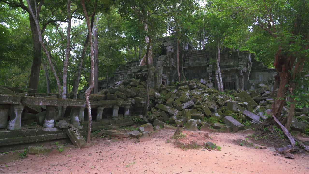 Angkor temple ruins surrounded by trees, stone columns, and carved archways in soft light, broken blocks covered with moss, dolly establish