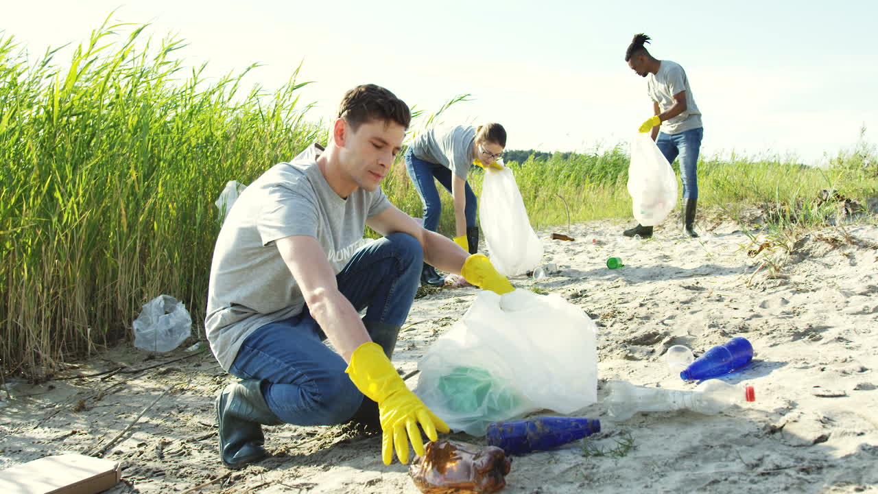 Close Upof The Young Man Collecting A Litter In The Plastic Bag And Then Smiling To The Camera At The Lake