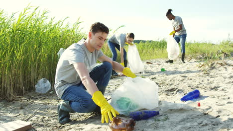 close upof the young man collecting a litter in the plastic bag and then smiling to the camera at the lake