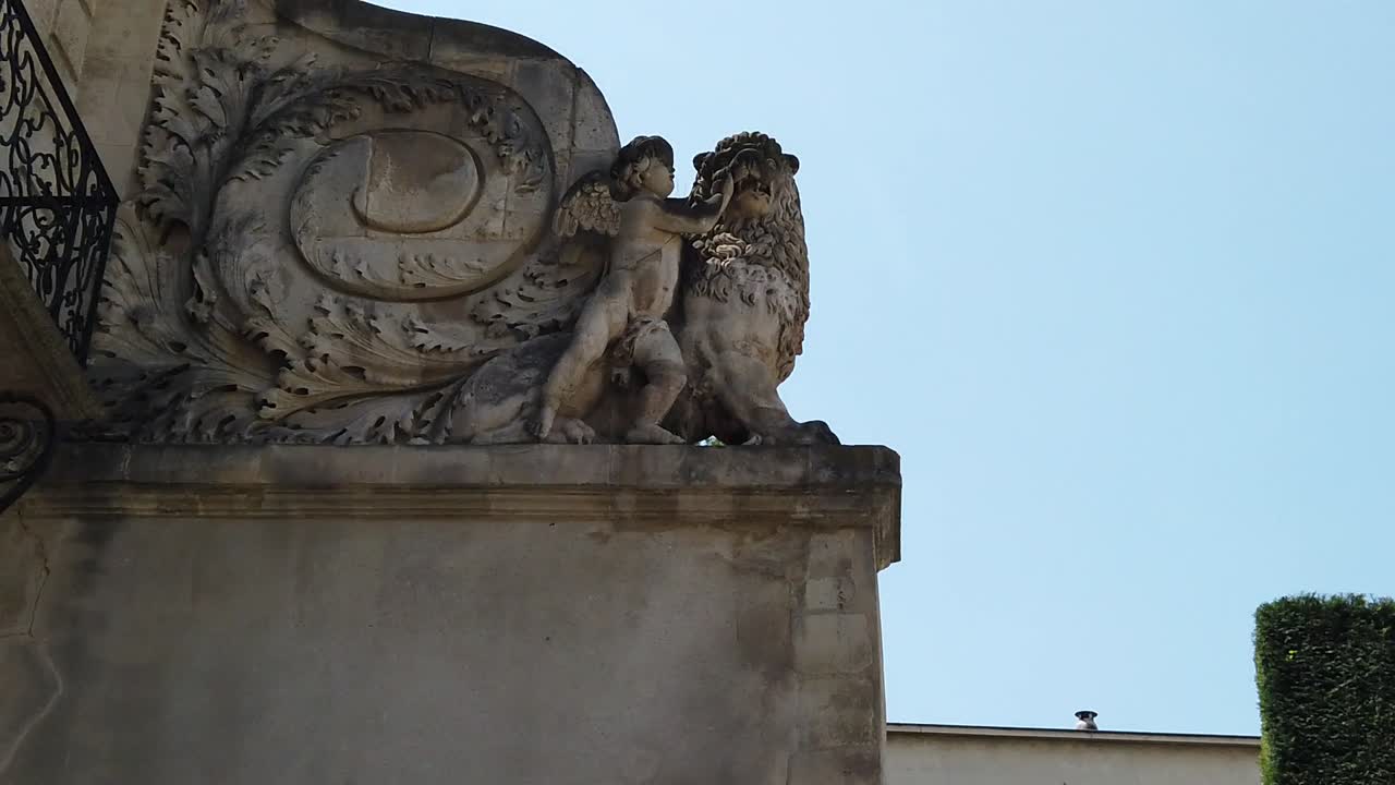 Primo piano di una scultura in pietra ornata che raffigura un leone e una figura umana sulla facciata di un edificio storico in Marocco, con dettagli architettonici intagliati sullo sfondo di un cielo azzurro limpido.