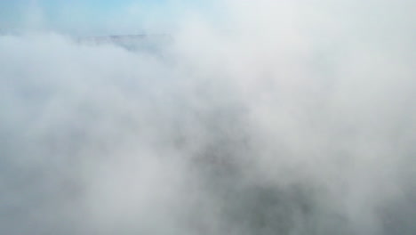 aerial view through a thick, white fog cloud above the sea on a sunny morning