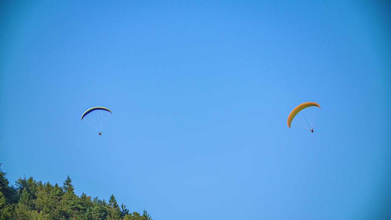 Two adventurous paragliders against blue sky on sunny day. Exciting sport