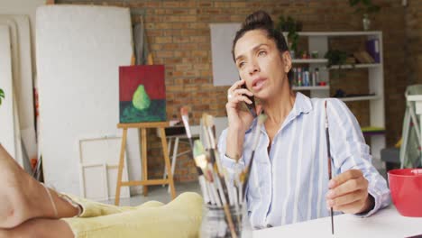 video de una feliz diseñadora biracial usando un teléfono inteligente en el estudio