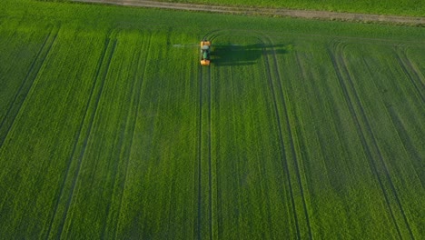 vista aérea de un agricultor rociando campos de cultivos con tractor, fumigación de pesticidas y fertilizantes, noche soleada de verano, luz de la hora dorada, tiro de drone ancho moviéndose hacia adelante, inclinado hacia abajo