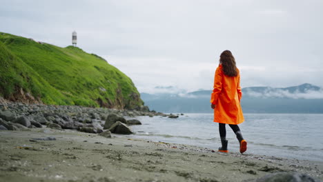 woman in orange raincoat walking on a beach