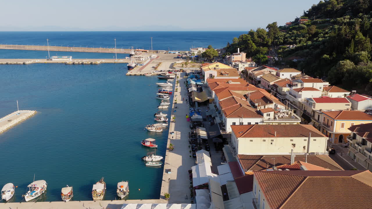 Ripresa aerea che sorvola il lungomare del porto di Katakolo, in Grecia, con caffè che costeggiano il lungomare e barche da pesca ancorate nella tranquilla baia