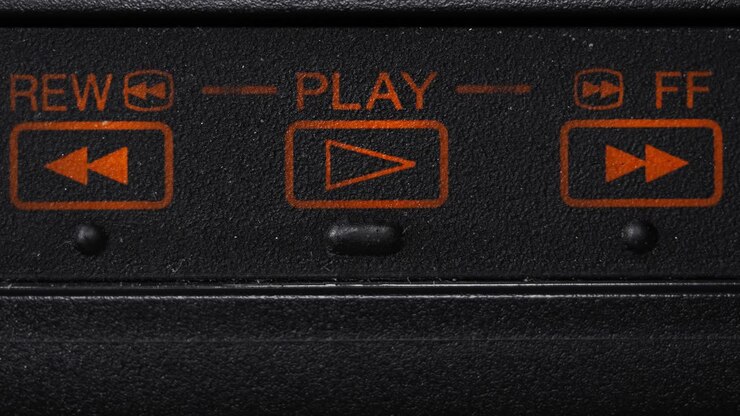 Primo piano di un dito che preme l'icona di riproduzione arancione su un videoregistratore retrò nero per avviare la riproduzione