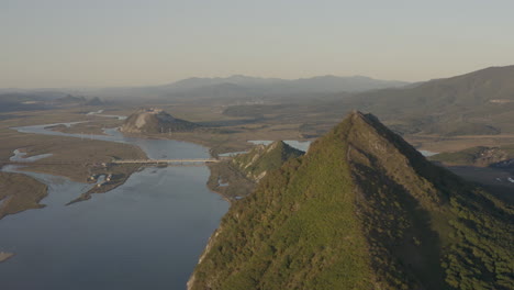 Vista-Del-Paisaje-De-Un-Estuario-De-Río-Con-Dos-Montañas-En-Forma-De-Pirámide-Y-Una-Cresta-De-Montaña-En-El-Fondo-De-La-Puesta-De-Sol