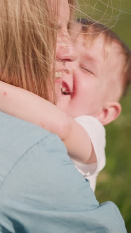 A woman in a blue dress bends down to embrace her son,who hugs her blissfully with a big smile on his face. tender moment of love and connection between mother and child in a sunny, green grass field