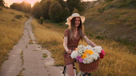 una chica con un vestido montando una bicicleta con flores en una canasta y riendo disfrutando de la libertad y el aire de verano. cámara lenta.