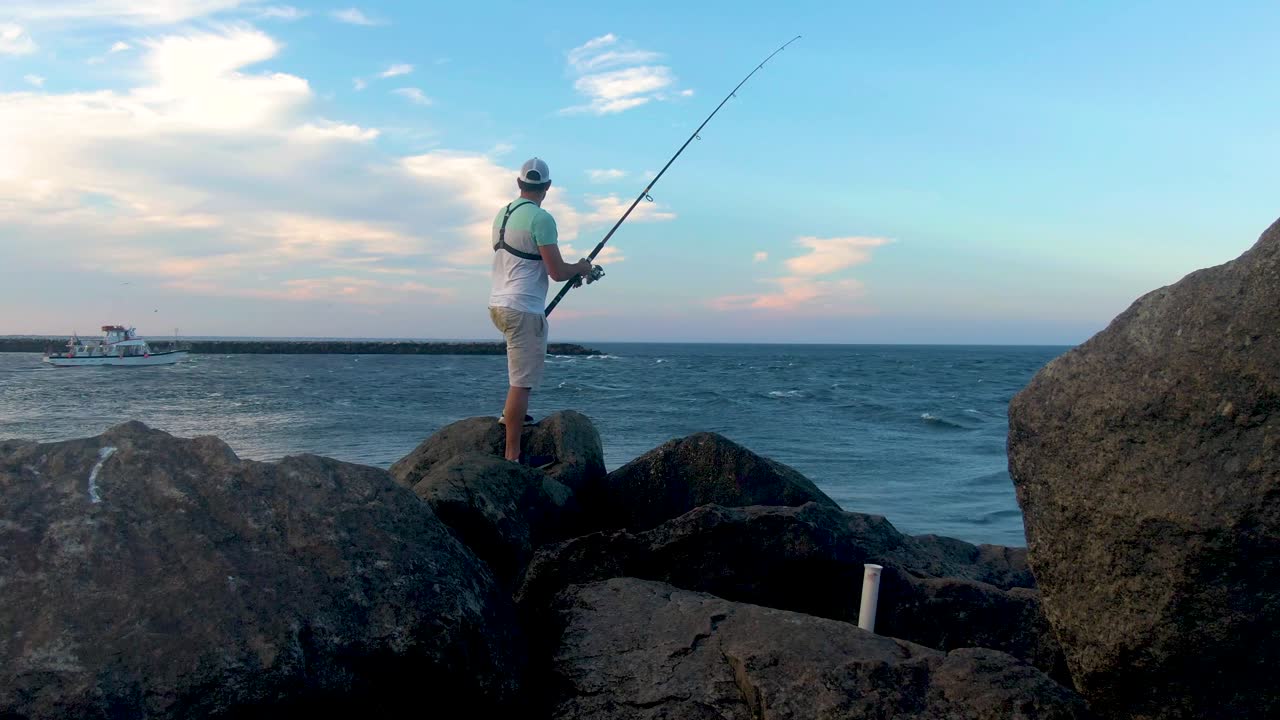 Pria muda memancing teknik spin di garis pantai laut, dilihat dari belakang.