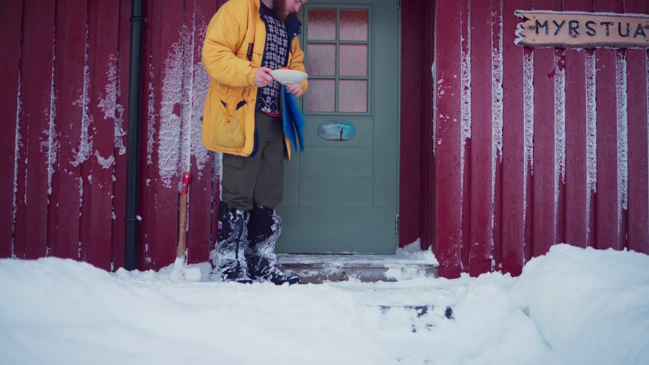 Man With Fruits In Plate Come Out Of The Cabin Door And Sits On The Ground In Winter