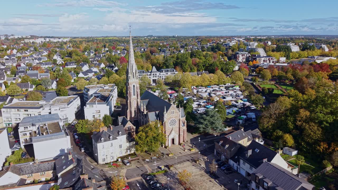 Drone shot flying forward toward Saint-Martin Church in Cesson-Sévigné, France, on a sunny day with surrounding trees and residential buildings