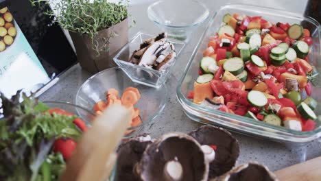 Chopped-vegetables-in-baking-dish,-chopping-board-and-ingredients-on-kitchen-worktop,-slow-motion