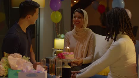 Multi-Cultural-Friends-Giving-Woman-Birthday-Cake-With-Candles-At-Party-At-Home
