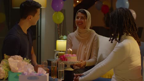 amigos multiculturales dando a la mujer pastel de cumpleaños con velas en una fiesta en casa