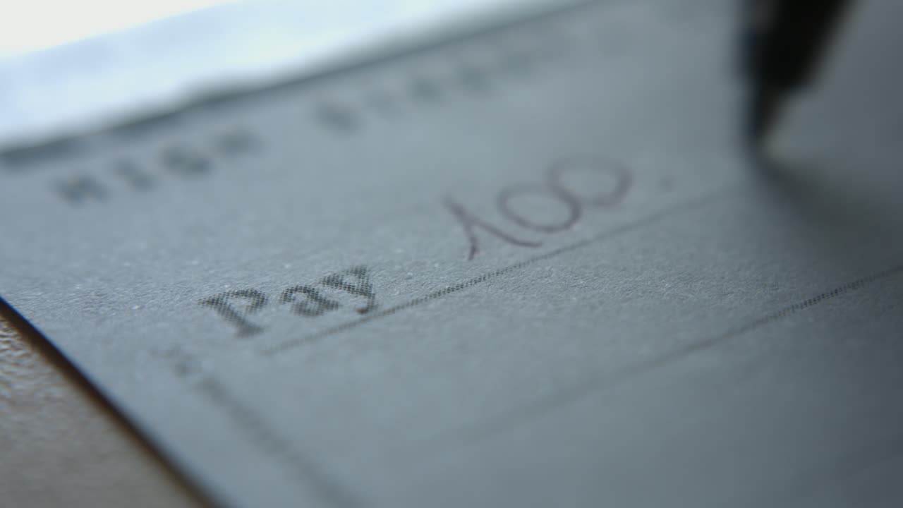 Primo piano di una mano che scrive cento dollari su un assegno