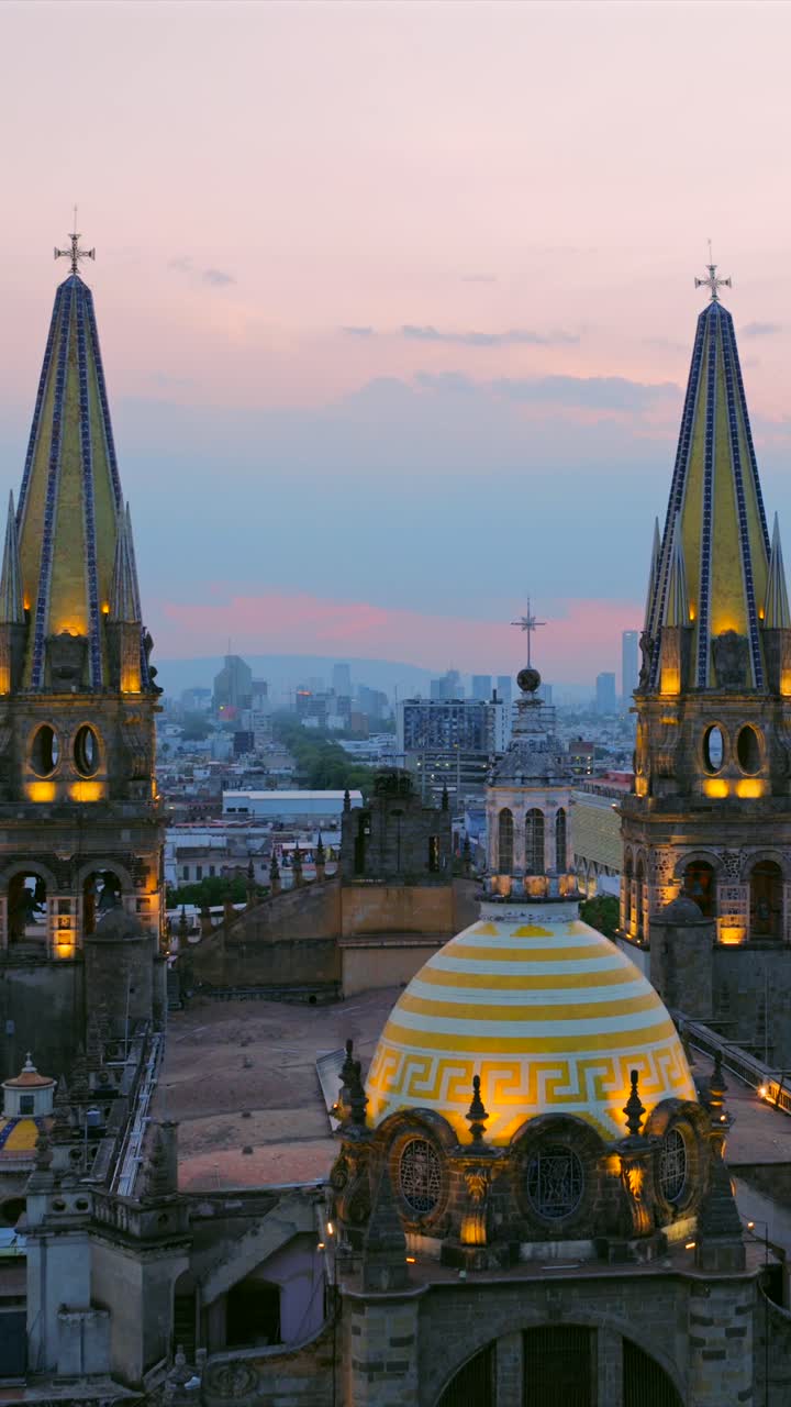 Close up flyover of illuminated Guadalajara Cathedral spires and dome, reveals the Guadalajara city skyline at dusk. Drone aerial dolly in