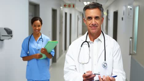 Portrait-of-smiling-doctors-with-medical-reports-standing-in-corridor
