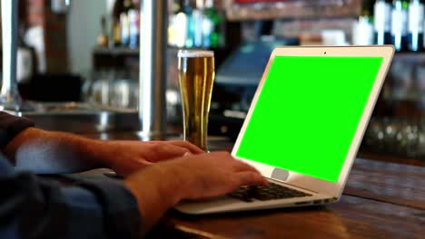 Customer-using-a-laptop-with-green-screen-at-bar-counter