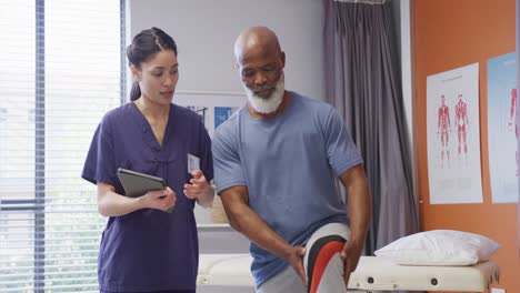 Diverse-female-physiotherapist-and-senior-male-patient-holding-knee-during-physical-therapy-session