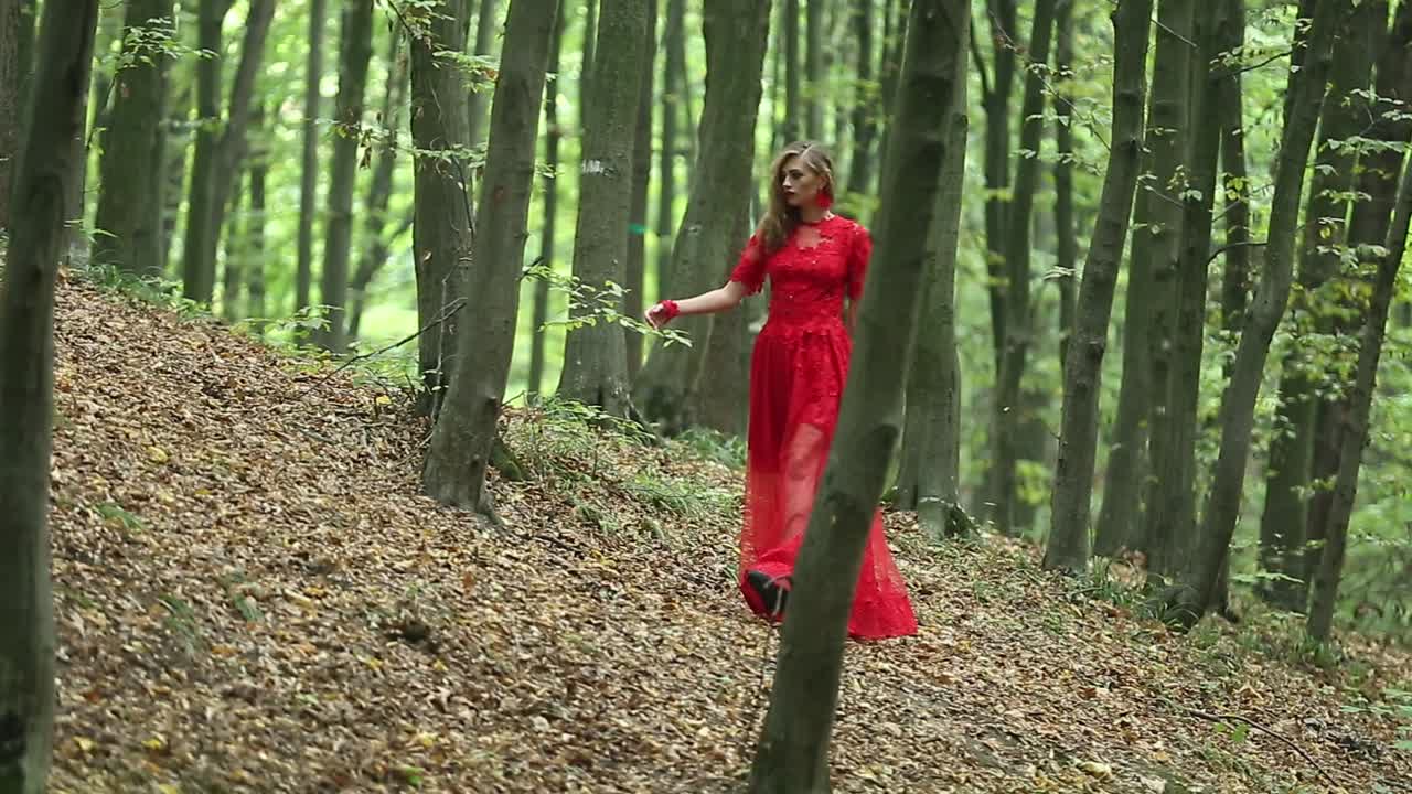 Beautiful Woman Walking Through Green Forest. Beautiful woman in red long dress walking through green forest