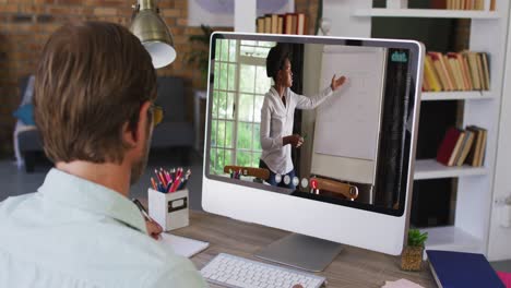 Caucasian-male-teacher-taking-notes-while-having-a-video-call-with-female-teacher-on-computer