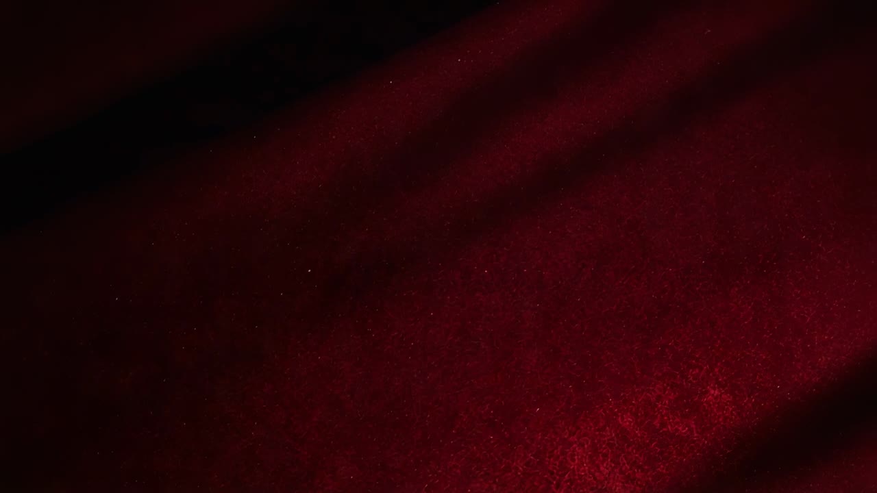 Luce che si sposta rivelando un primo piano di un tessuto in peluche rosso intenso, con bande d'ombra diagonali e macchioline