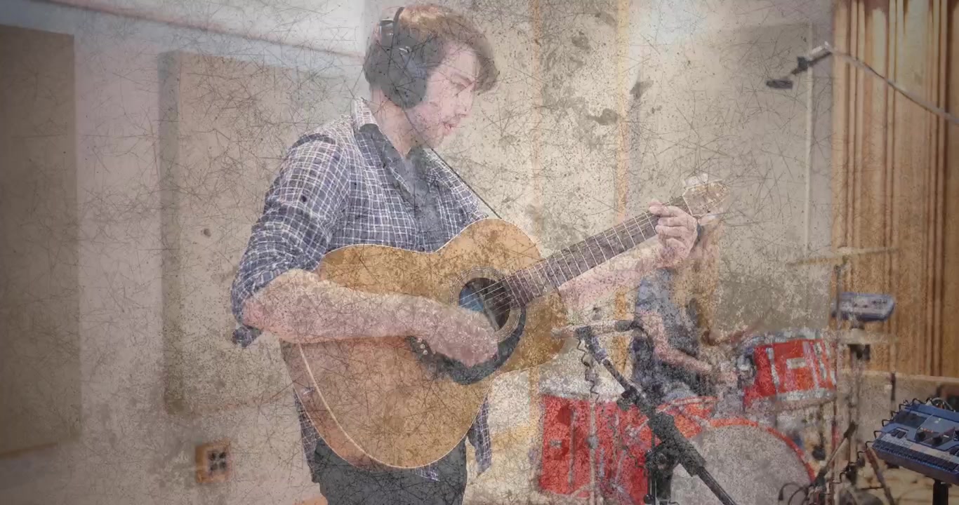 Müzik stüdyosunda erkek gitarist gitarını hazırlayıp akorları çalarken, kadın davulcu ritim ekliyor.