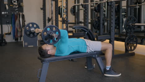 guy inside the gym doing lying triceps extension exercises, stimulating the entire triceps muscle group