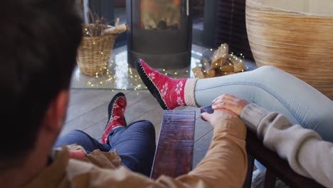 vista trasera de una pareja cogida de las manos mientras está sentada cerca de la chimenea en la casa de vacaciones