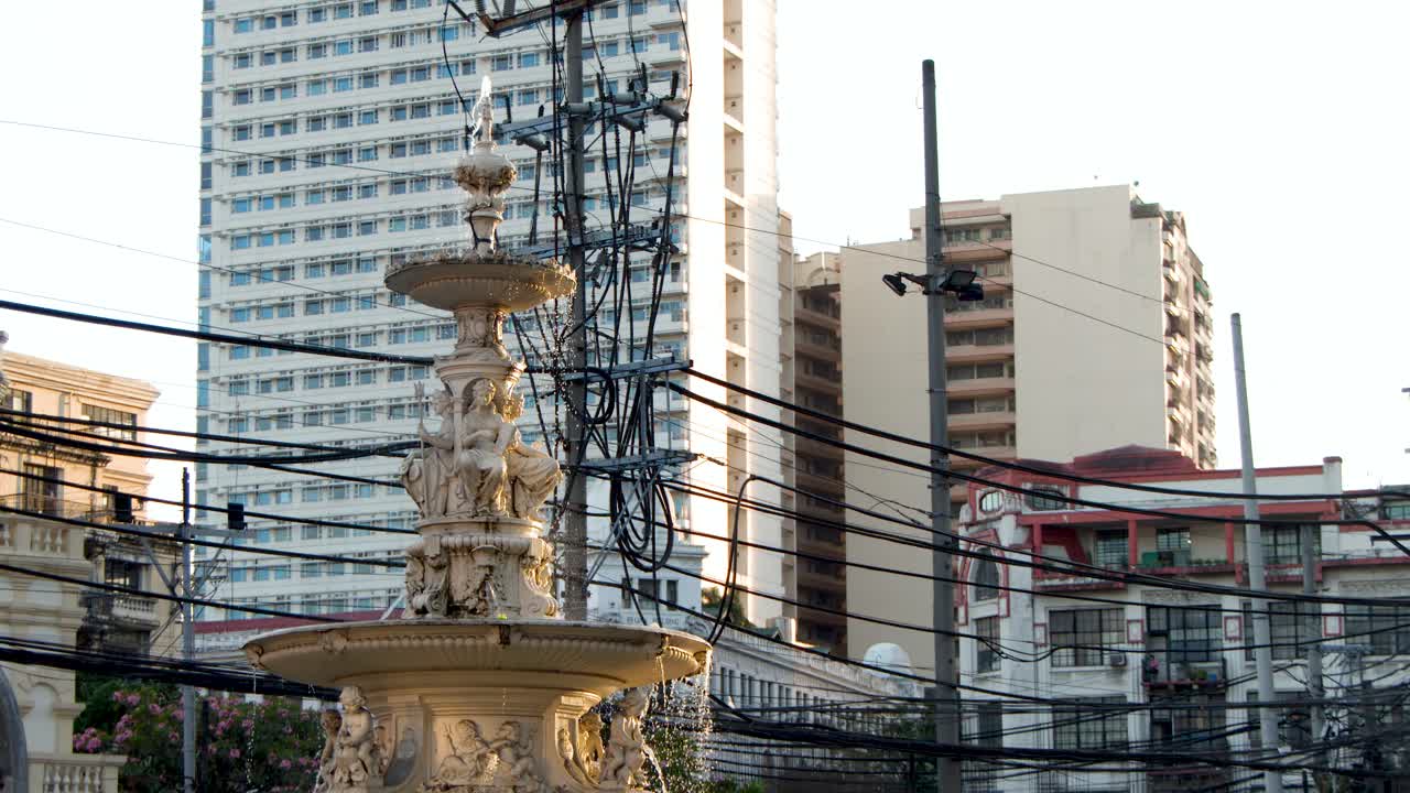 Plano general fijo de una iglesia histórica y una fuente entre el tráfico urbano y los cables eléctricos.