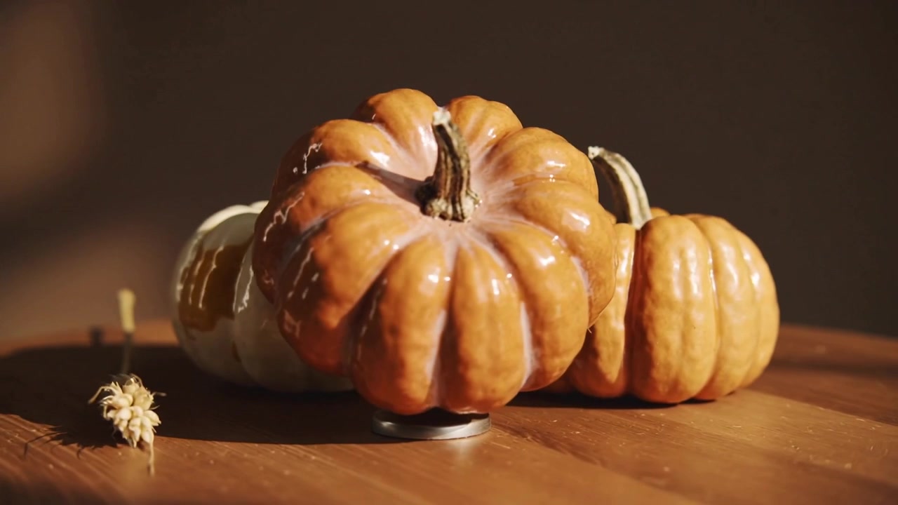 Rotating base moving orange pumpkin forward, covering white pumpkin on wood table, showing pumpkin